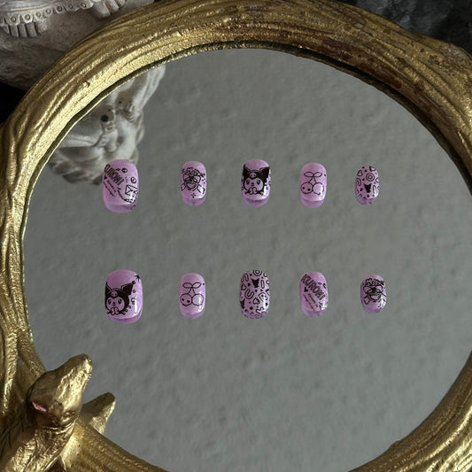 Handmade Kuromi-inspired purple press-on nails with lilac jelly base, black line art, cherries, skull doodles, and kawaii gothic motifs. Cute pastel punk nail design for Sanrio fans.