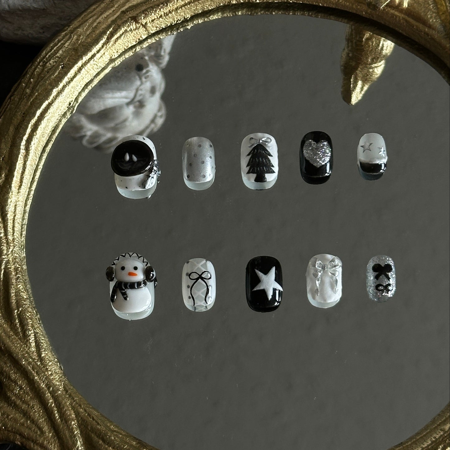 Black, white, and silver Christmas nails featuring a 3D snowman with headphones, silver chrome details, matte textures, bows, hearts, and holiday elements.