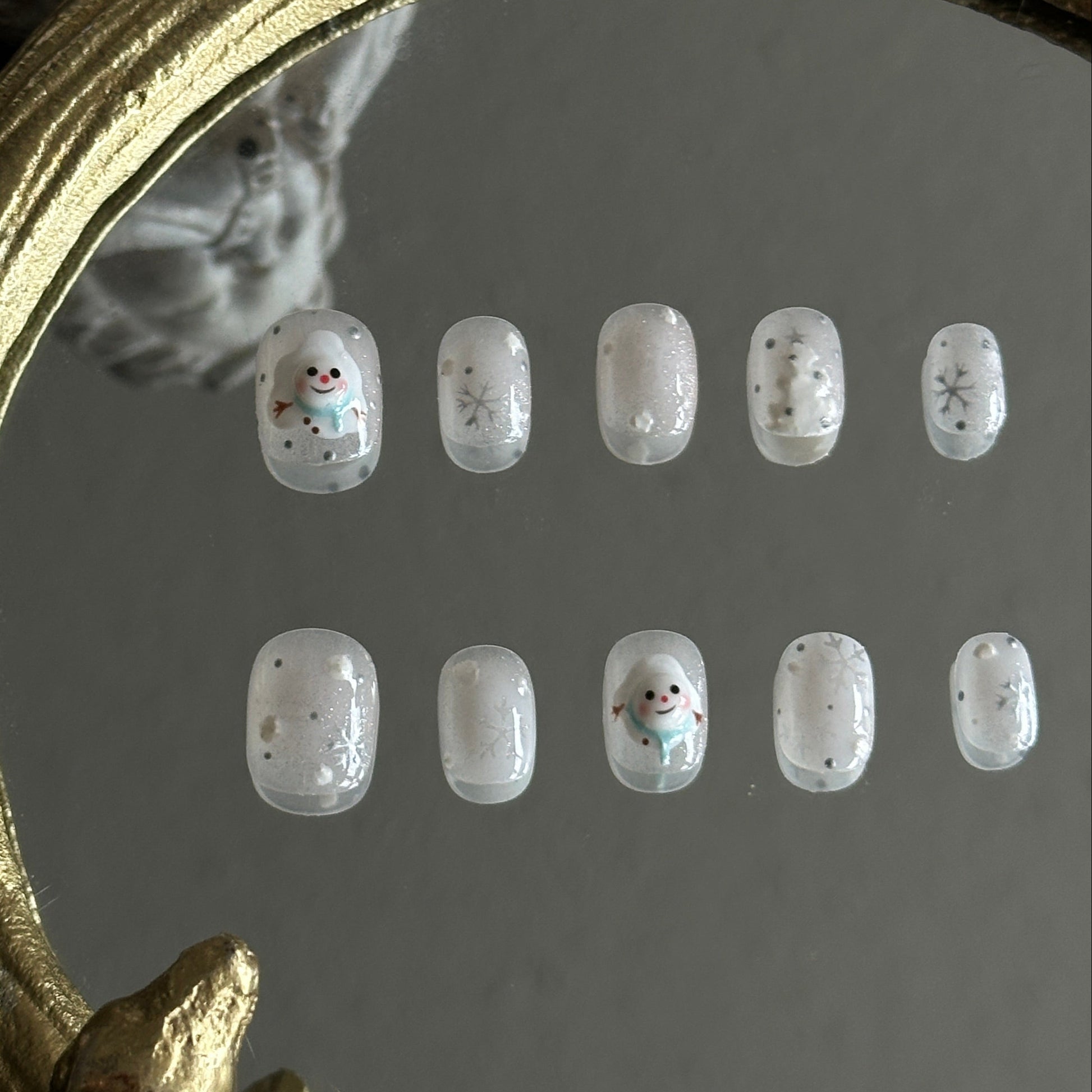 white ombre Christmas nails with glitter, a melting snowman in a blue scarf, snowflakes, and festive winter details.