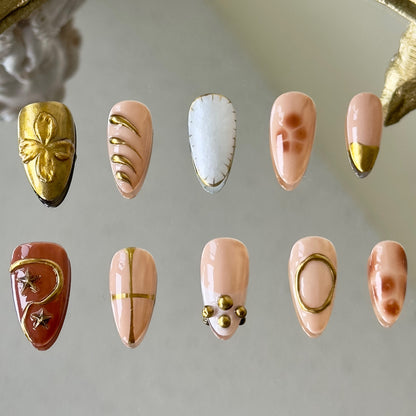 Front view of Auric nails with 3D gold chrome accents, brown floral smudges, and pearlescent white thread gel.