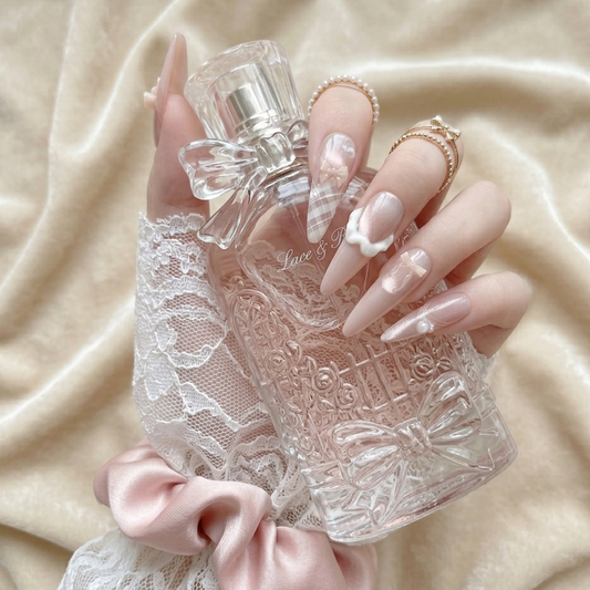 Lifestyle shot of Ballerina press-on nails by MYOB Nails, featuring almond-shaped soft pink nails with 3D cream bows, plaid patterns, and pearl accents, held against a vintage perfume bottle.