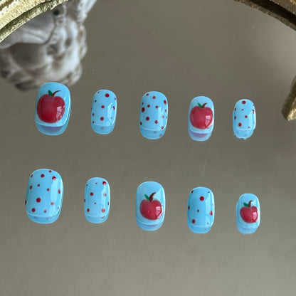 Front view of Bite Me handmade nails showing the playful combination of red polka dots and glossy apple art on blue.