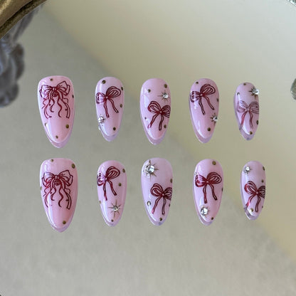 Front view of Bowberry handmade nails with metallic red bows and sparkling rhinestone accents.