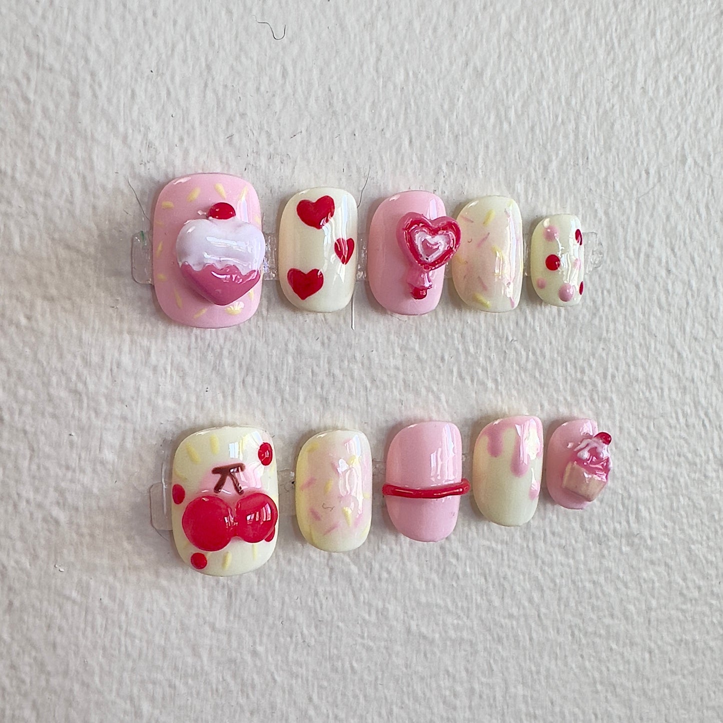 Detailed shot of the handcrafted 3D pink cupcake and glossy red cherry charms on a creamy yellow base.