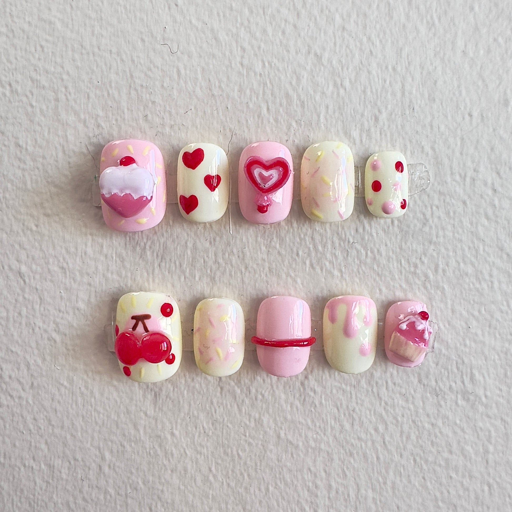 Front view of Cherry Cake nails showing the soft pink and pale yellow base with vibrant 3D charms.