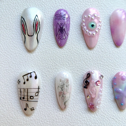 Close-up of MYOB Nails' handcrafted details featuring a minimalist hand-painted rabbit, a vintage angel sketch on purple lace, and a pink pearl-encrusted 3D evil eye charm.