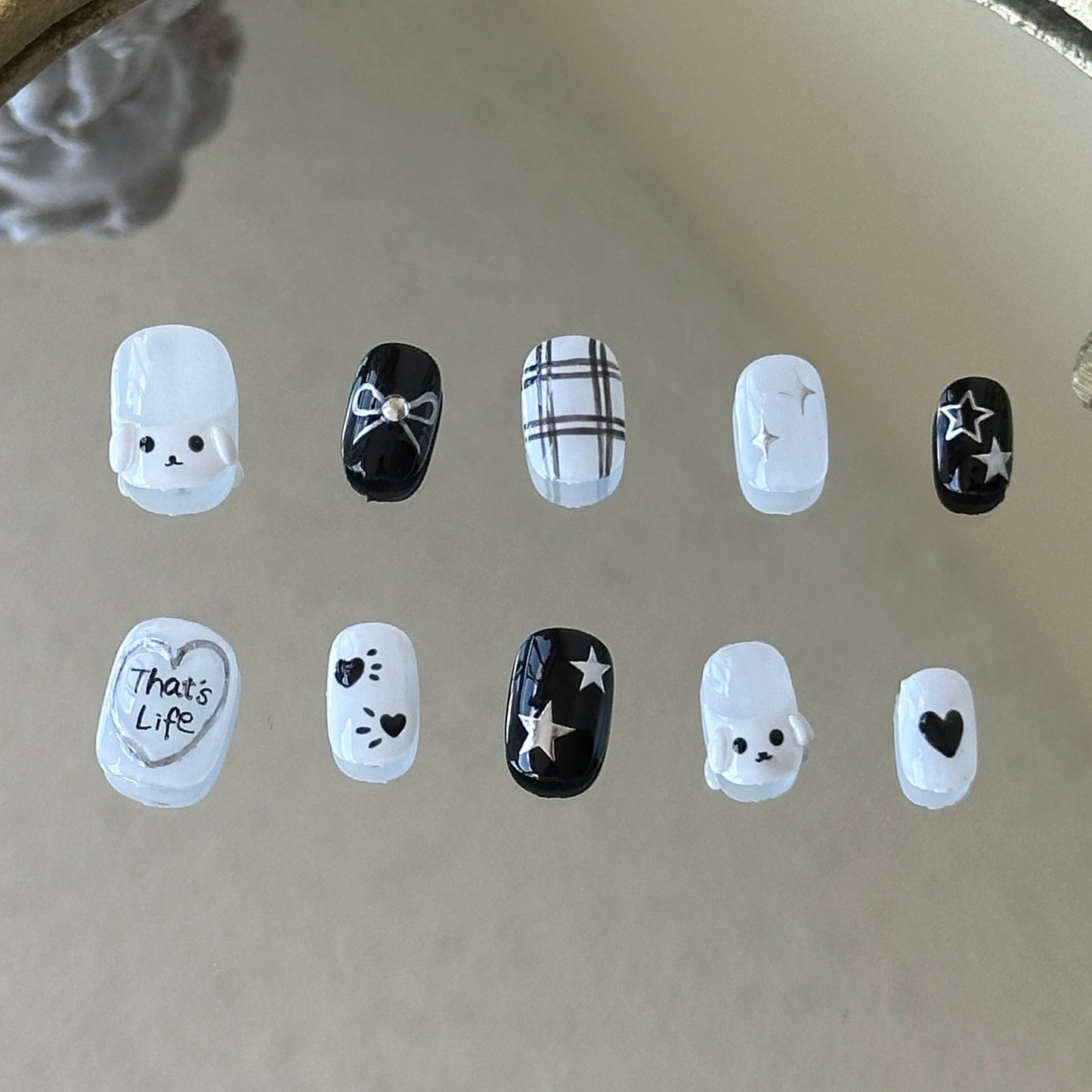 MYOB Nails handcrafted black and white press-on nails featuring 3D kawaii puppy charms, hand-painted plaid patterns, silver "That's Life" heart art, and dainty star doodles.