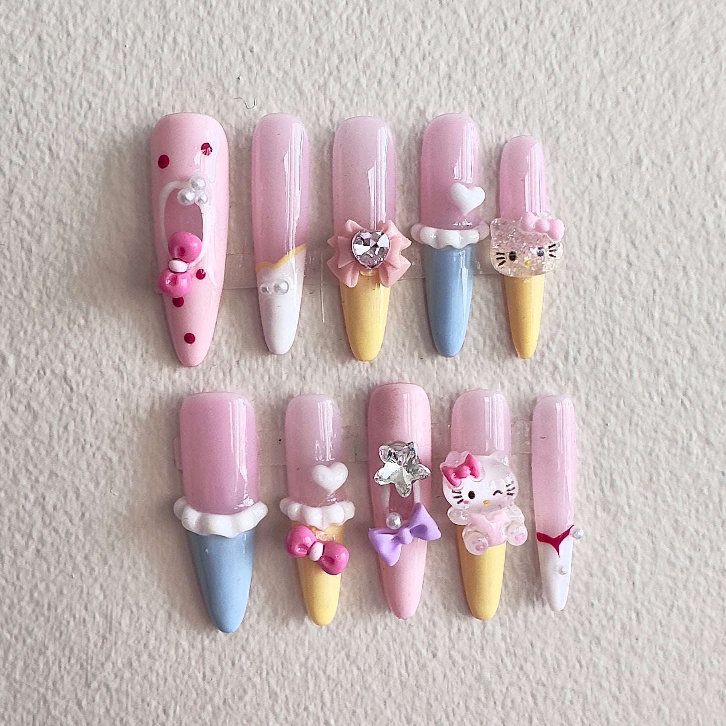 MYOB Nails vibrant dopamine-style press-on nails in pastel pink, yellow, and blue, featuring 3D ice cream cone designs, cute cartoon cat charms, pink bows, and heart accents.
