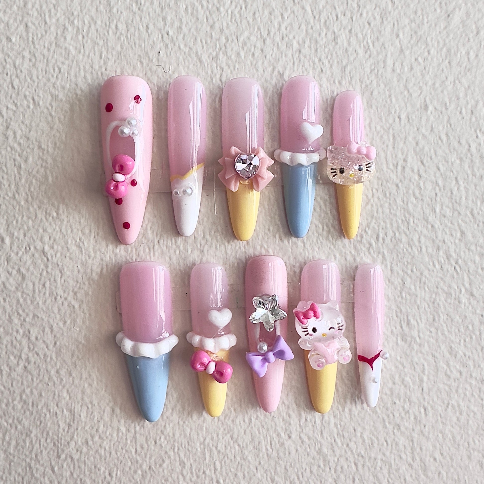 MYOB Nails vibrant dopamine-style press-on nails in pastel pink, yellow, and blue, featuring 3D ice cream cone designs, cute cartoon cat charms, pink bows, and heart accents.