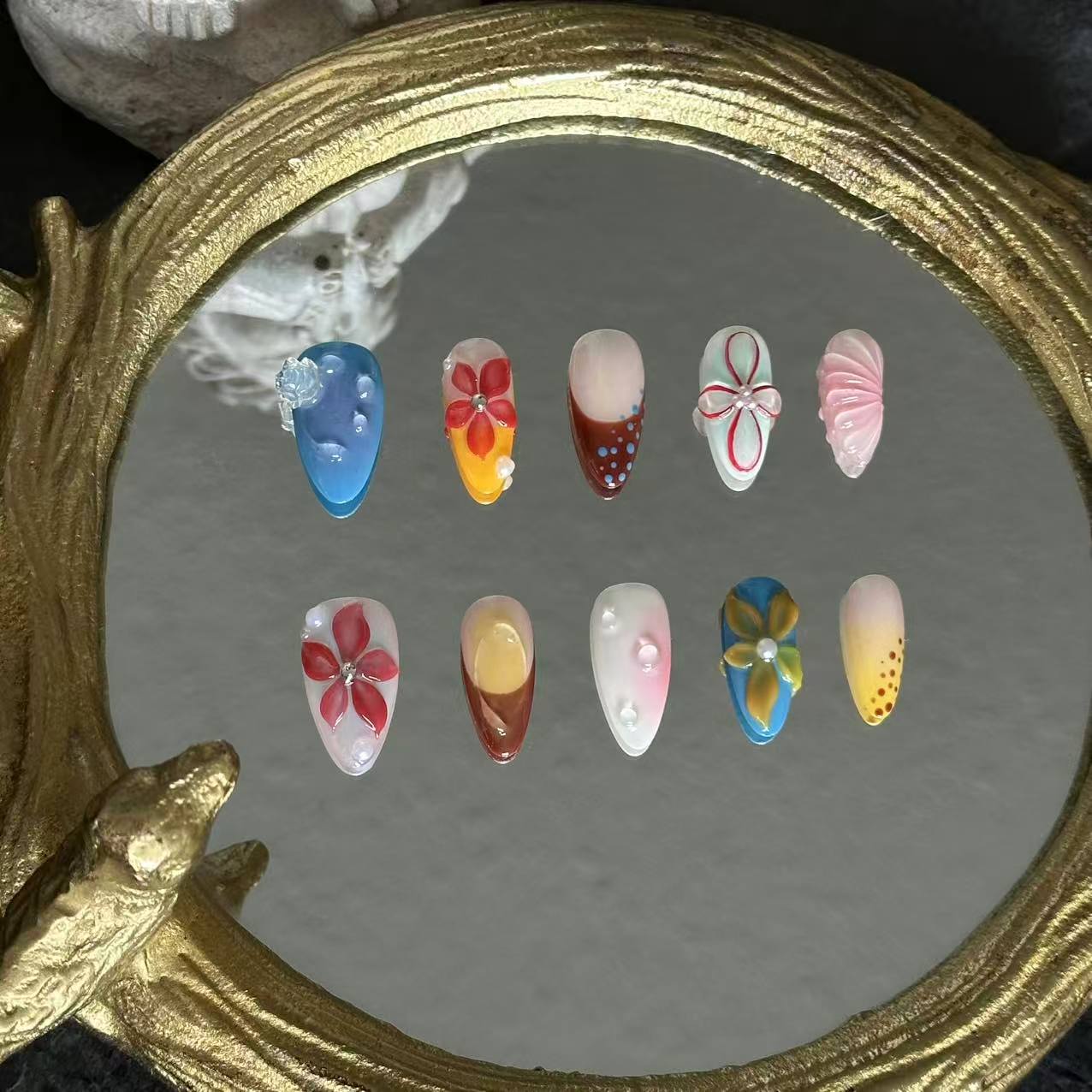 MYOB Nails Ethereal Bloom almond press-on nails, straight-on mirror flat lay, full layout of varied hand-painted floral designs, glossy nail finish and delicate gem embellishments
