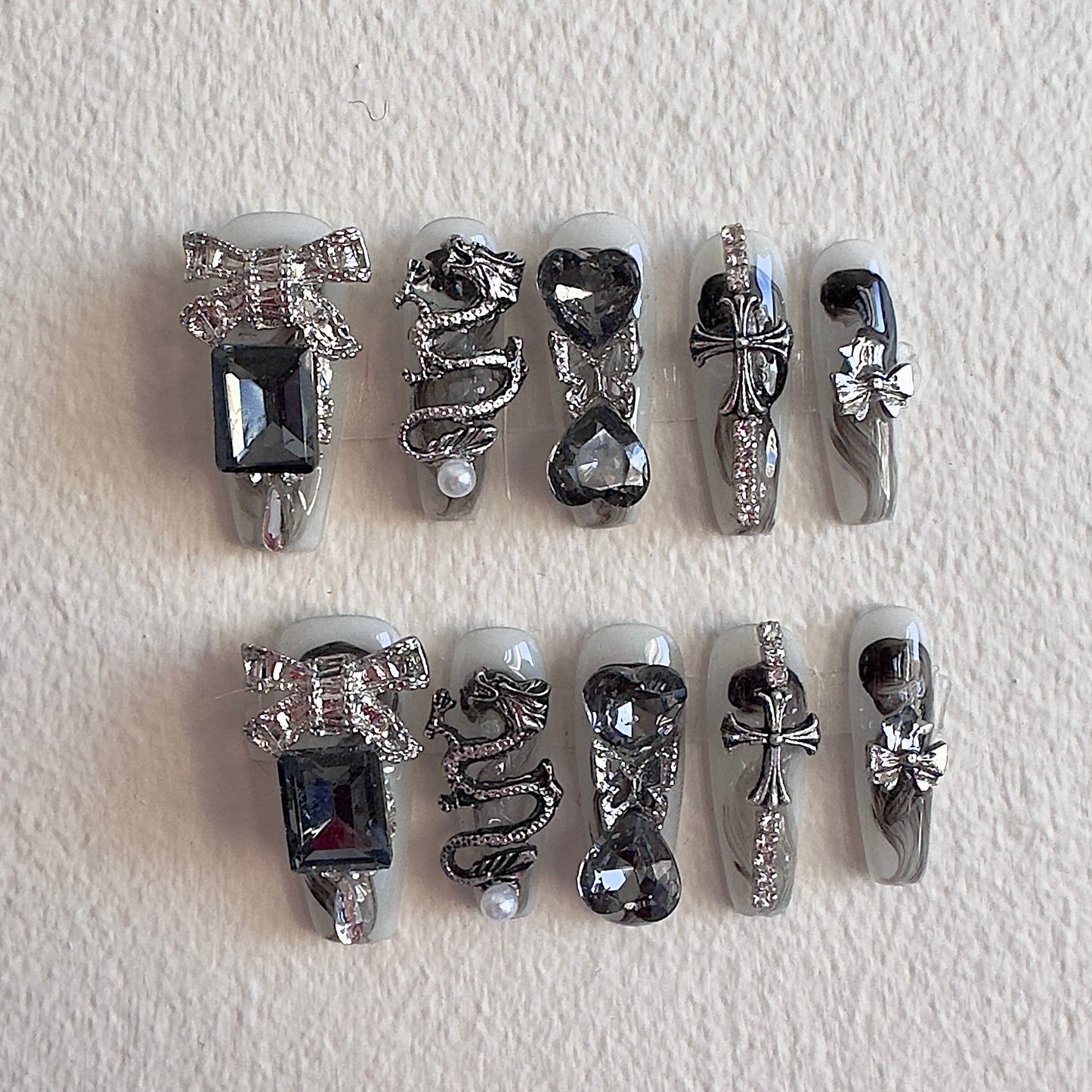 MYOB Nails gothic handmade press-on nails featuring a 3D silver dragon charm, metallic crosses, large black square gems, and edgy silver ribbon accents on a grey base.