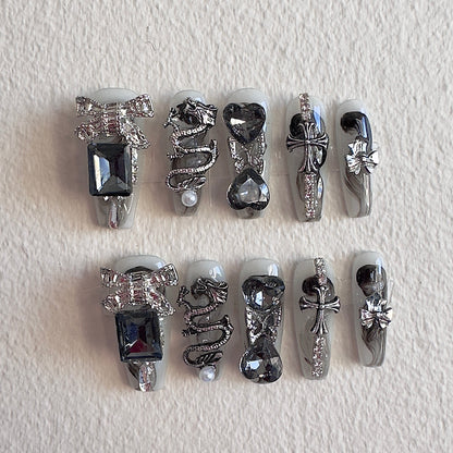 MYOB Nails gothic handmade press-on nails featuring a 3D silver dragon charm, metallic crosses, large black square gems, and edgy silver ribbon accents on a grey base.