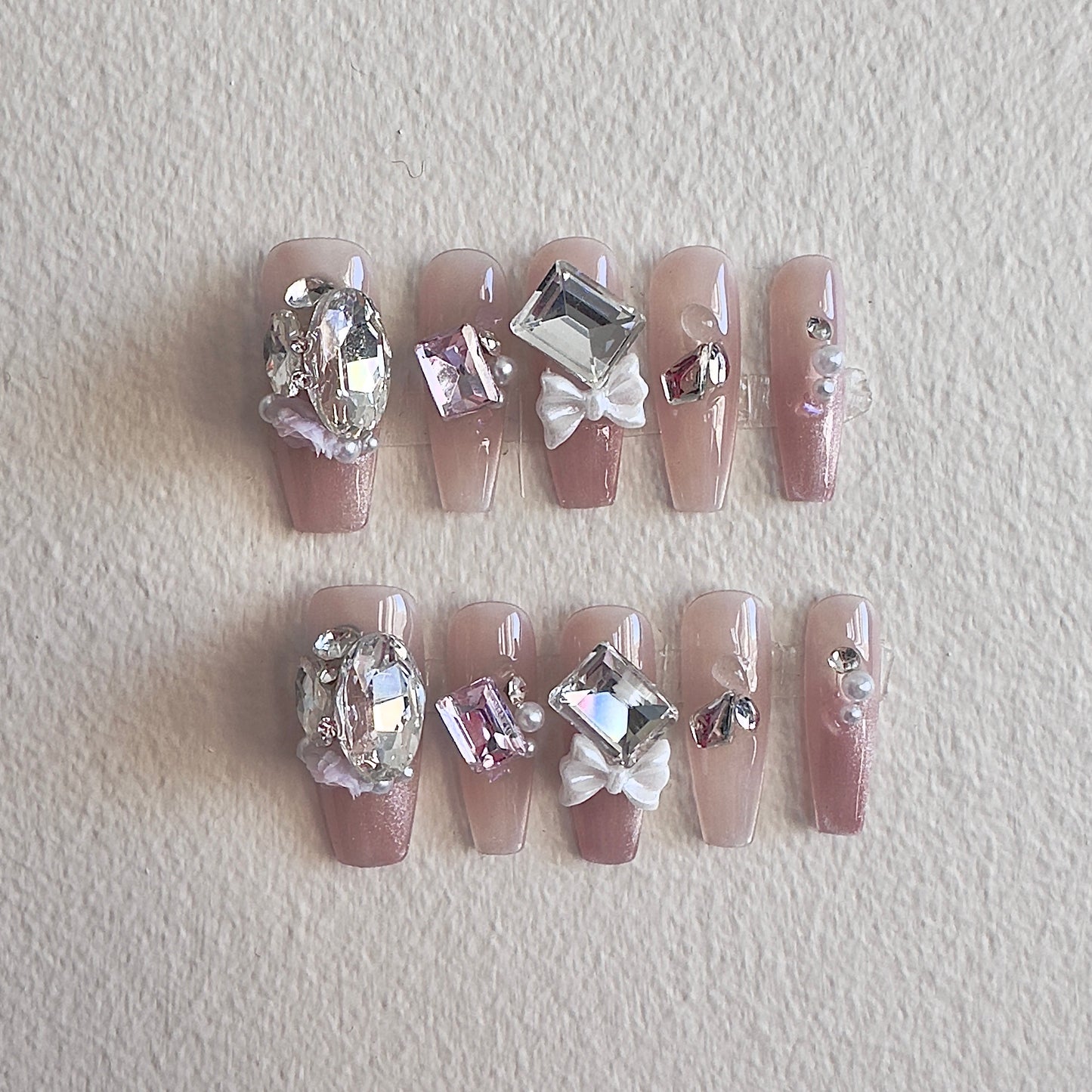 Handcrafted luxury press-on nails by MYOB Nails in shimmering nude pink, adorned with oversized geometric crystals, white 3D bows, and delicate pearl accents.
