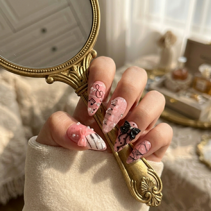 Hand model holding a vintage gold mirror showcasing MYOB Nails Melody Muse set with pink glitter, black lace patterns, and 3D ribbon accents for a coquette aesthetic.