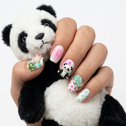 MYOB Nails Panda-monium press-on nails featuring 3D panda charms, pink polka dots, and floral accents, held by a hand model with a plush panda toy.