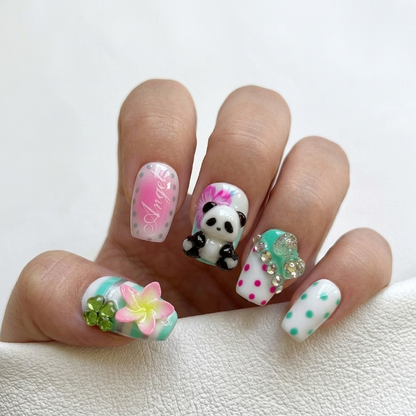 Detailed view of MYOB Nails Panda-monium set featuring 3D panda charms, pink "Angel" lettering, rhinestone accents, and colorful polka dots on a hand model.