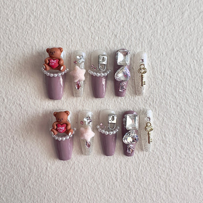 MYOB Nails elegant purple press-on nails featuring 3D brown bear charms, pearl borders, sparkling crystals, and vintage gold key accessories.