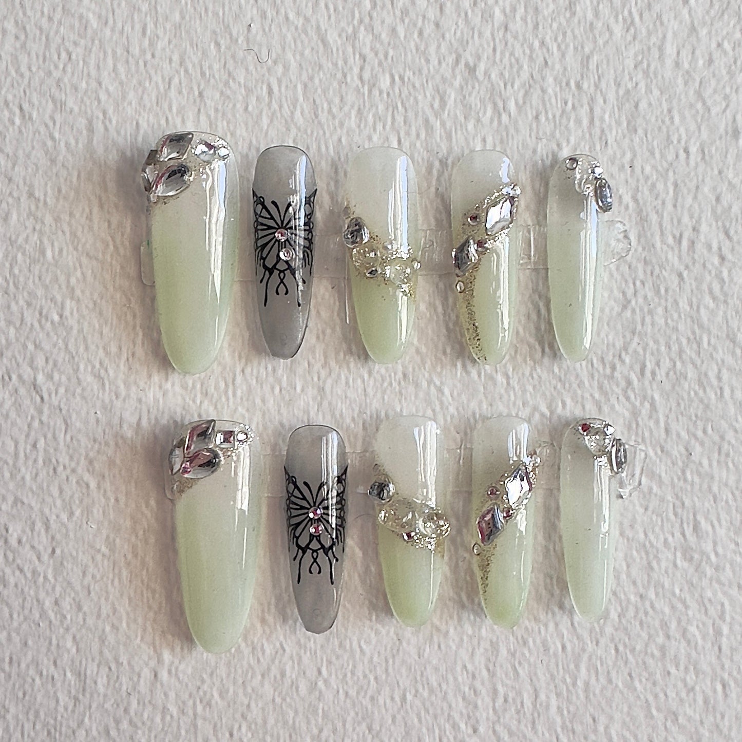 MYOB Nails Y2K aesthetic press-on nails with translucent light green base, featuring bold black butterfly art, dazzling crystal clusters, and glittery diagonal accents.