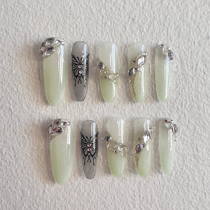 MYOB Nails Y2K aesthetic press-on nails with translucent light green base, featuring bold black butterfly art, dazzling crystal clusters, and glittery diagonal accents.