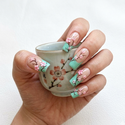 Close-up of MYOB Nails Zen Blossom set showing 3D floral art on almond nails, held by a hand model with a traditional oriental tea cup.