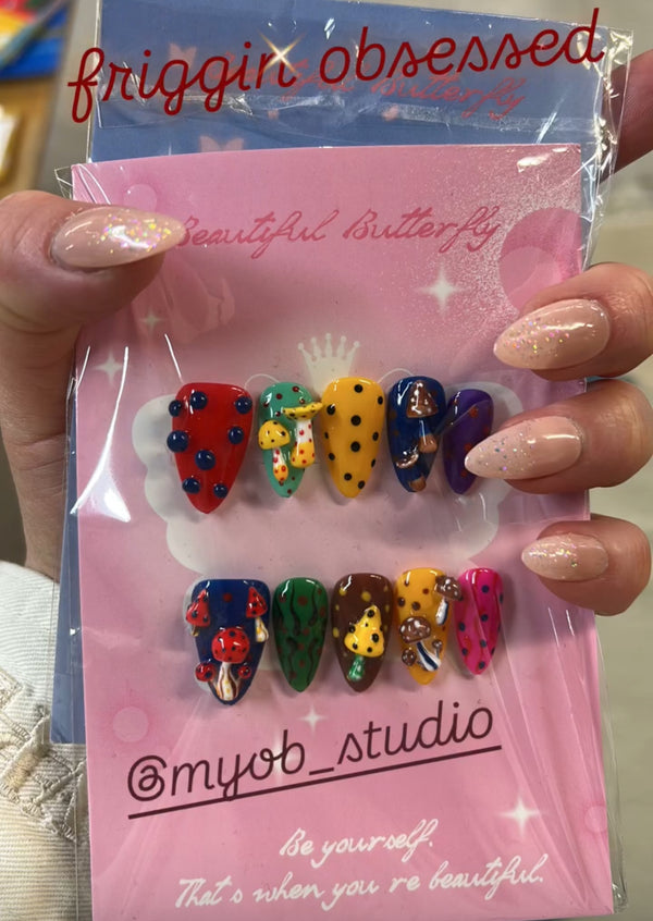 a photo from client wearing a solid color pink set holding another mushroom nail set, both are from myobnails