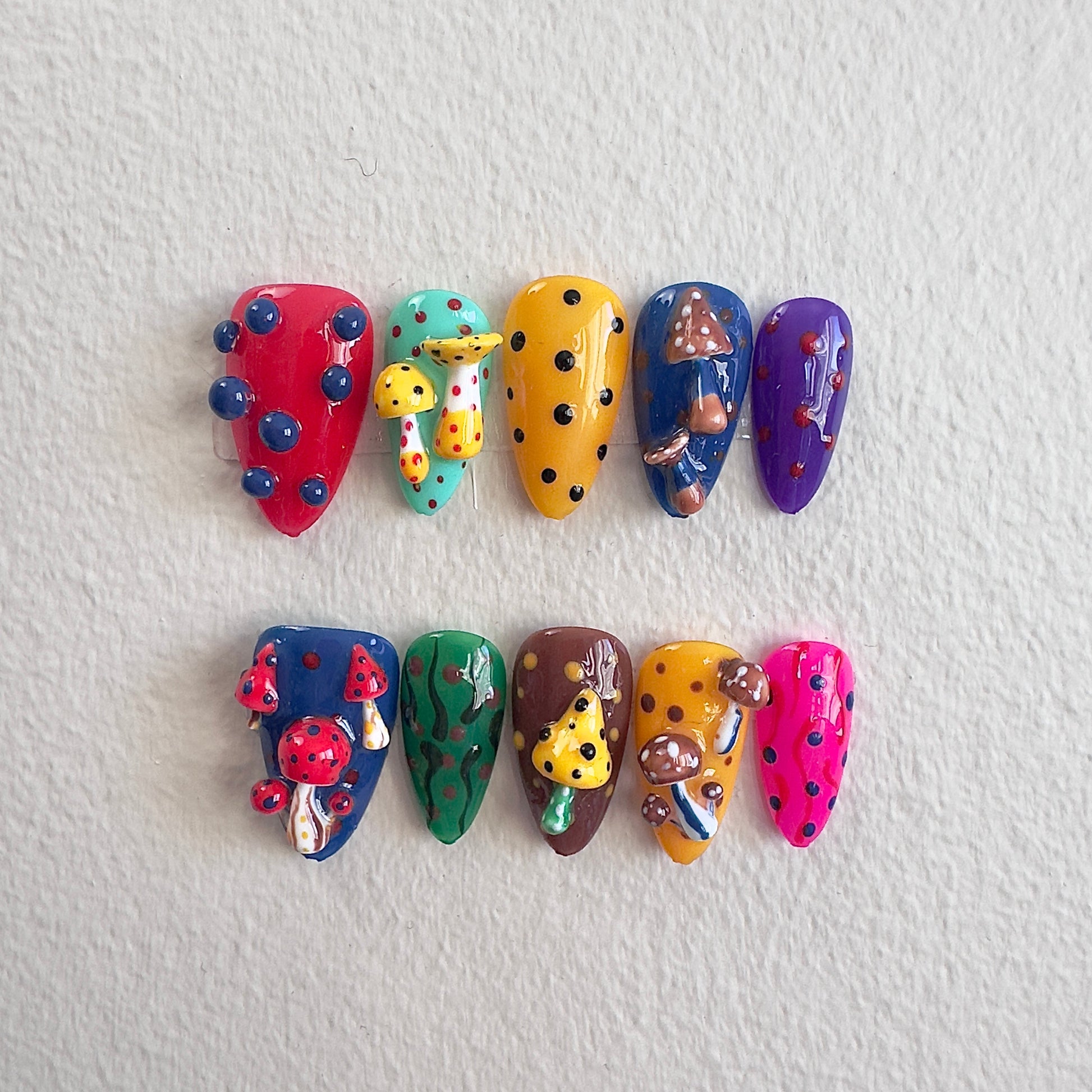 Front view of Mystic Shroom nails showing the vibrant multi-colored base and whimsical 3D forest elements.