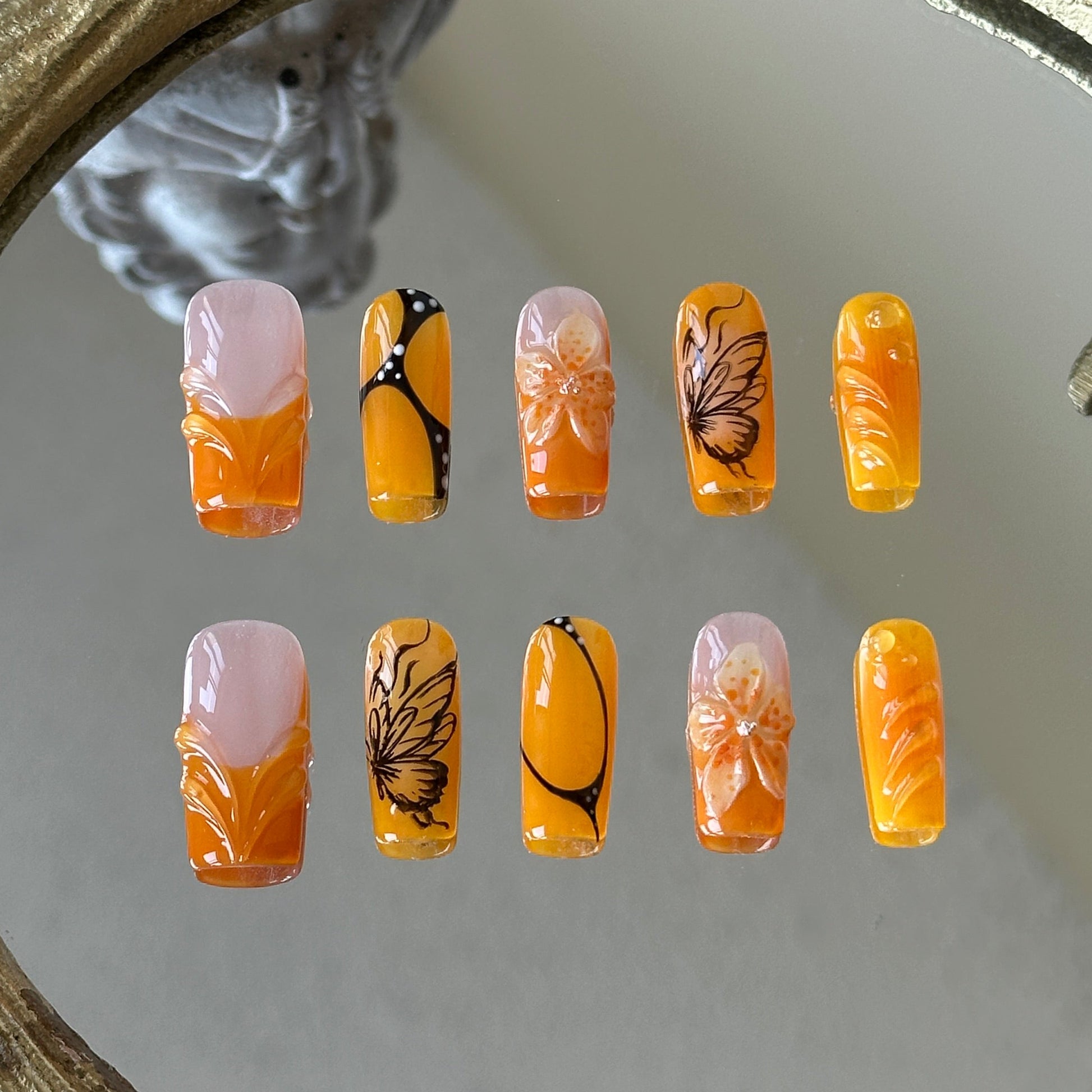 Front view of Orange Sunset handmade nails with orange French tips and intricate butterfly wing textures.