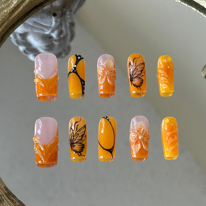 Front view of Orange Sunset handmade nails with orange French tips and intricate butterfly wing textures.