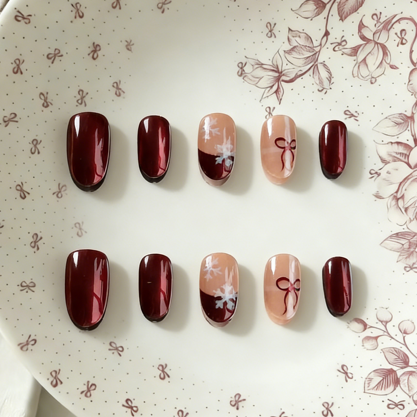 Ruby Snow press-on nails by MYOB Nails, featuring a festive design with deep red chrome powder finish, delicate white snowflake art, and red bow motifs on nude accent nails.