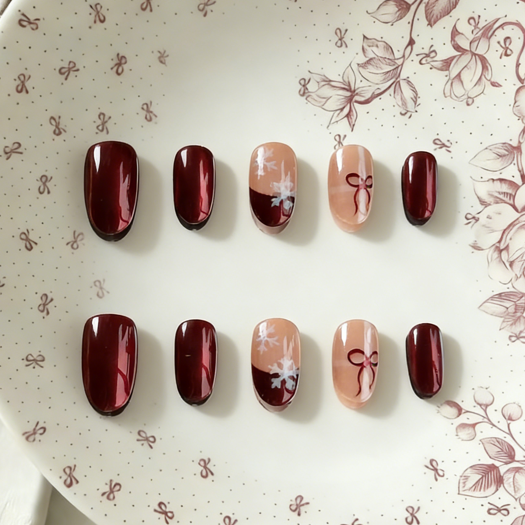 Ruby Snow press-on nails by MYOB Nails, featuring a festive design with deep red chrome powder finish, delicate white snowflake art, and red bow motifs on nude accent nails.