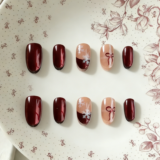 Ruby Snow press-on nails by MYOB Nails, featuring a festive design with deep red chrome powder finish, delicate white snowflake art, and red bow motifs on nude accent nails.