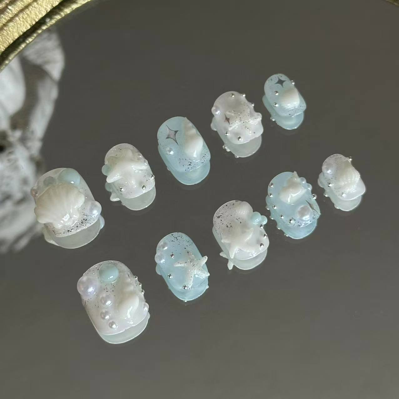 A macro shot of Siren's Treasure by MYOB Nails, showcasing the exquisite 3D white scallop shell and lustrous pearl accents nestled on a shimmering blue base.